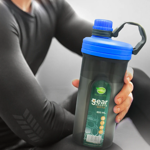 A person is holding a Gear Sports Bottle (850ml) with a blue cap. The bottle is in the person's hand while he is dressed in a black athletic outfit, with a blurred background.