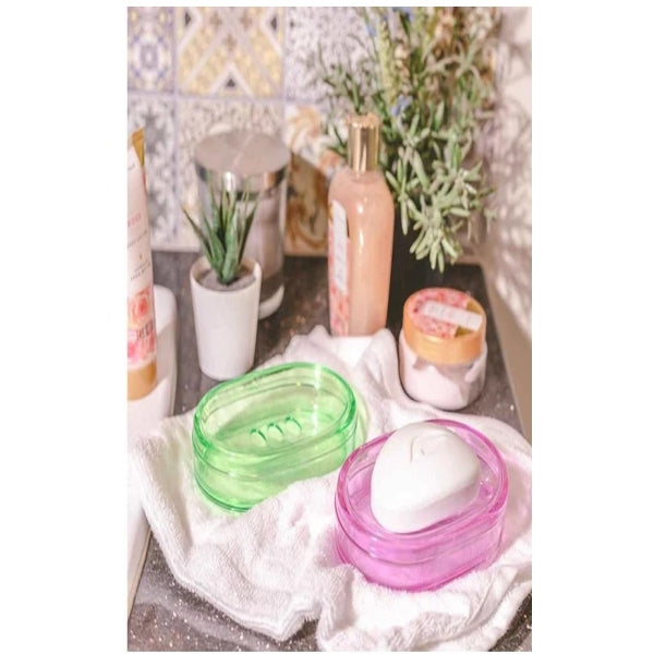 Pink and green soap dishes with soap inside, placed on a towel with bathroom essentials in the background.