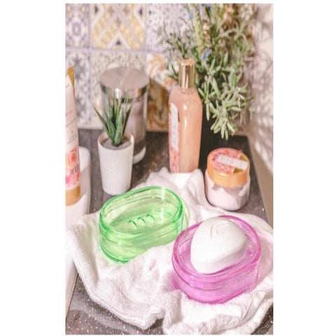 Pink and green soap dishes with soap inside, placed on a towel with bathroom essentials in the background.