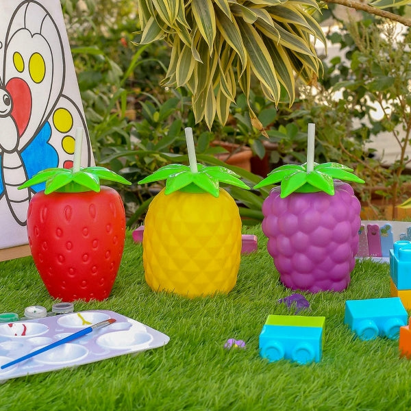 Colorful fruit tumblers in strawberry, pineapple, and raspberry shapes with green tops and straws, ideal for fun outdoor drinks for children